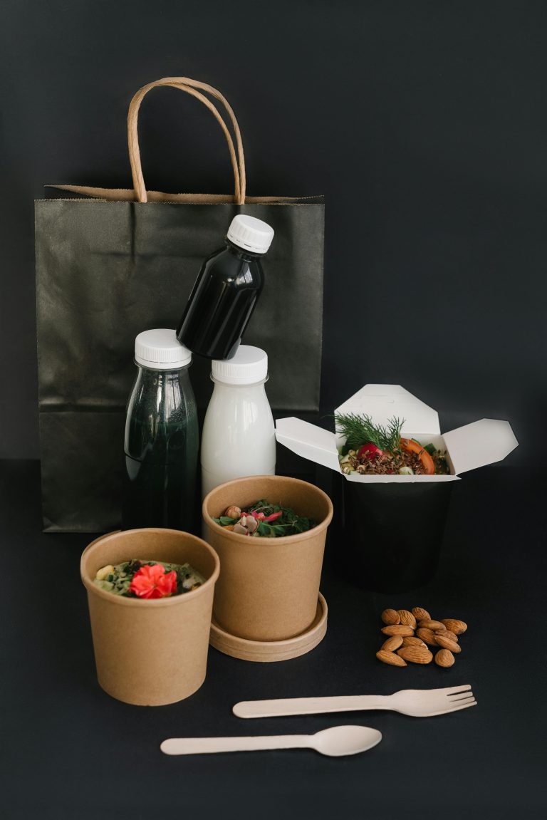 A collection of eco-friendly food containers and bottles on a black surface, highlighting sustainable takeaway options.